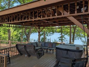 A covered deck with a seating area, a hot tub, and a view of a lake.