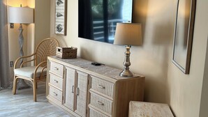 Une pièce comprenant un fauteuil en osier, une armoire en bois, un téléviseur à écran plat et un miroir au mur.