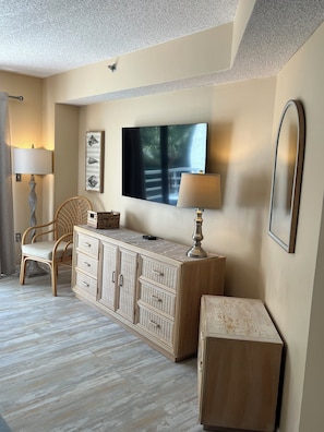 A room with a wicker chair, a wooden cabinet, a flat-screen TV, and a mirror on the wall. - Stunning Oceanfront Villamare- You'll Love it Here! (Hilton Head Island)