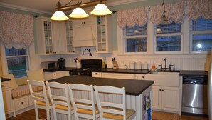 A kitchen with white cabinetry, a central island, and a dining area with white chairs. - Trackside Home- Walk to Everything (Track, Town, SPAC) (Saratoga Springs)