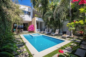 A swimming pool surrounded by lush greenery and a modern building with a balcony.