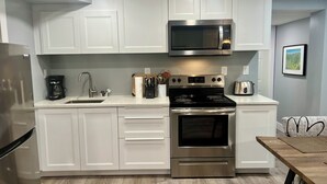 A modern kitchen with white cabinets, a stainless steel microwave, a stove, and a sink.