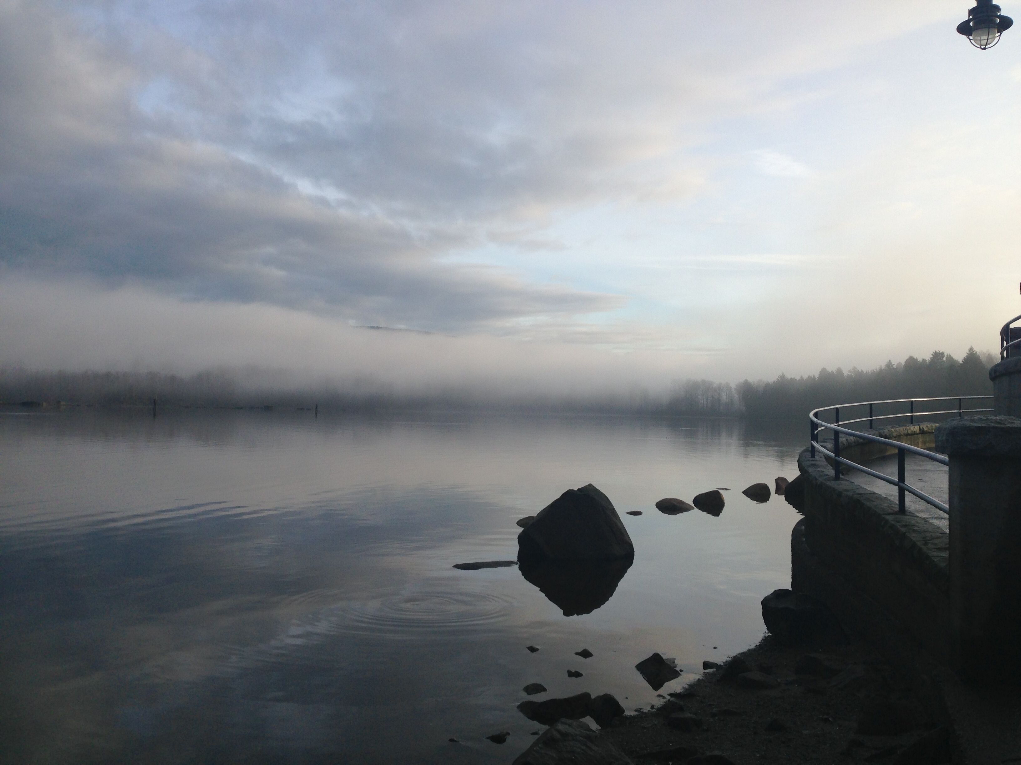 A calm lake with a stone structure and a metal railing on the right.