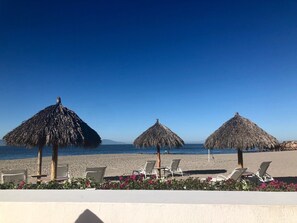 Un espace de détente aménagé sur la plage, avec des parasols en chaume et des chaises longues.