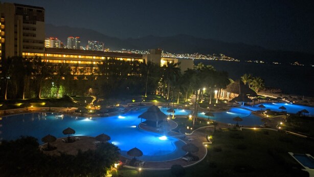 A resort with multiple swimming pools, palm trees, and a city skyline in the background. - Paradise at Shangrila, Beachfront (Puerto Vallarta)