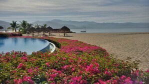 A beach resort with a swimming pool surrounded by pink flowers, beach chairs, and umbrellas. - Paradise at Shangrila, Beachfront (Puerto Vallarta)