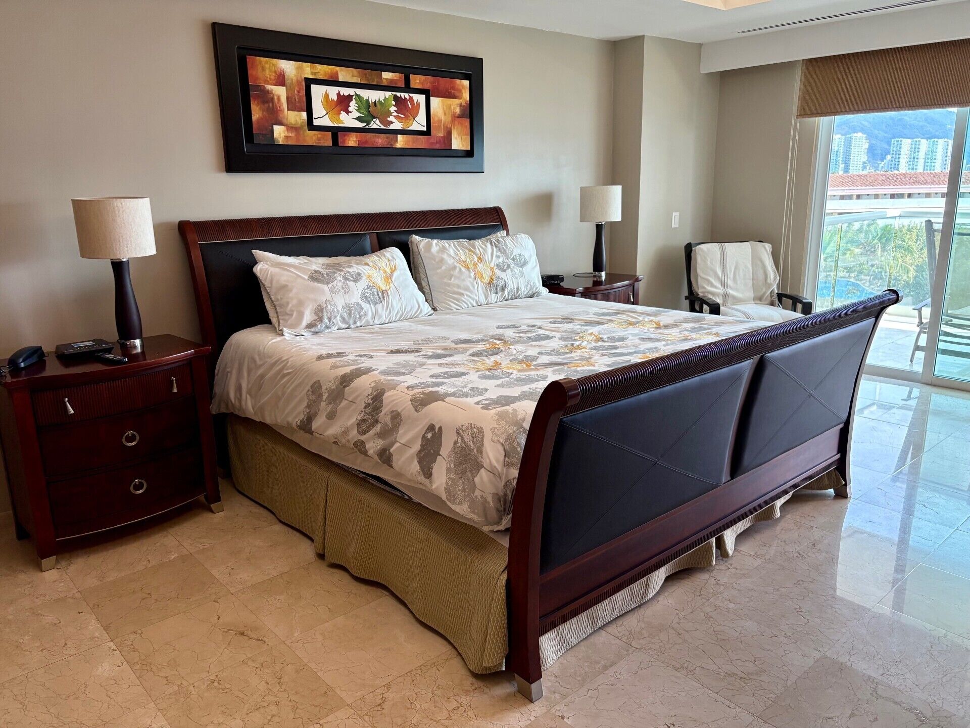 A hotel room with a large bed, two bedside tables with lamps, a framed artwork on the wall, and a view of the outside.