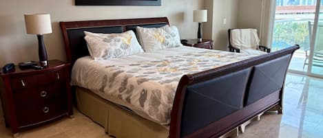 A hotel room with a large bed, two bedside tables with lamps, a framed artwork on the wall, and a view of the outside.