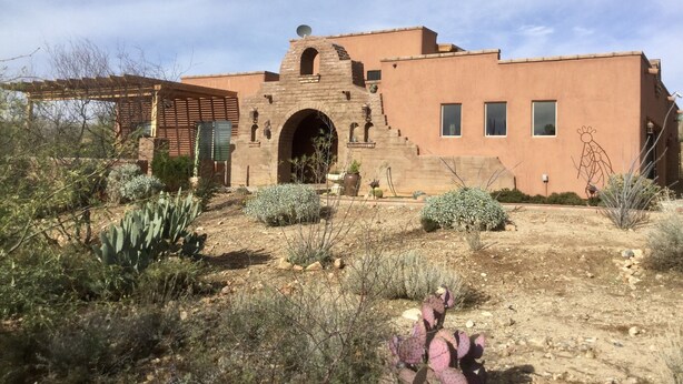 A building with a distinctive arched entrance and a flat roof, surrounded by desert vegetation. - Unique, Custom Built Studio for your Private Peaceful Retreat (Green Valley)