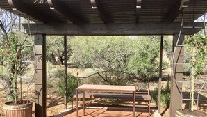 An outdoor patio with a wooden table and benches, surrounded by potted plants and a pergola structure. - Unique, Custom Built Studio for your Private Peaceful Retreat (Green Valley)