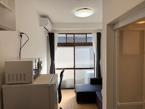 A room with a bed, a desk, an air conditioning unit, a window with curtains, and a door.