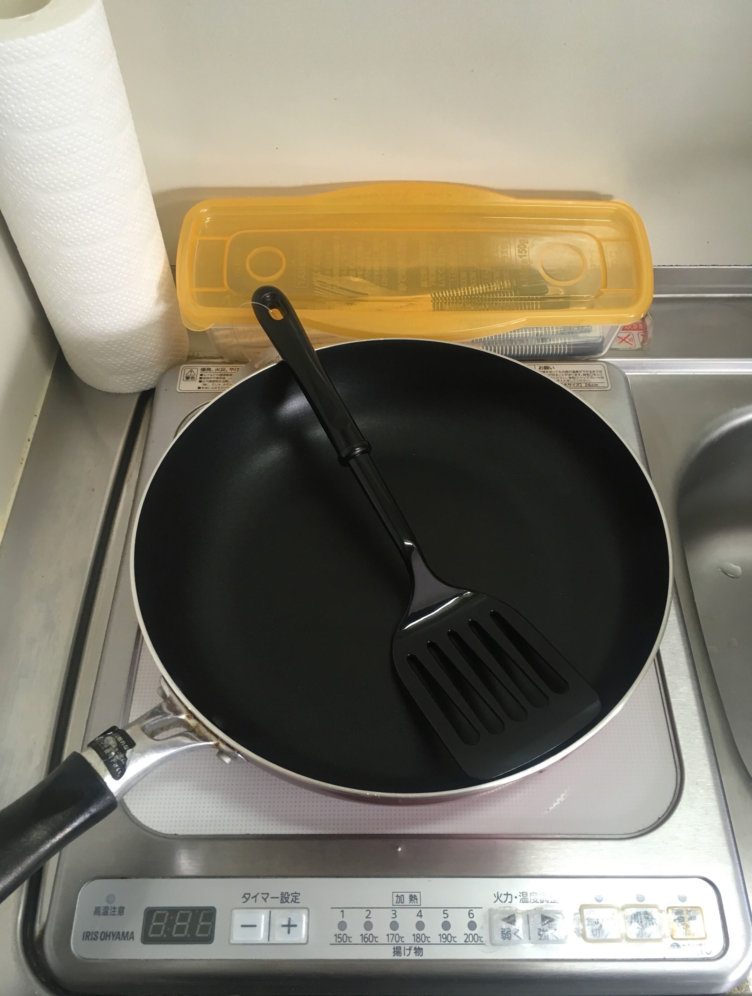 A kitchen with a frying pan on an induction cooktop, a paper towel roll, and a yellow container.