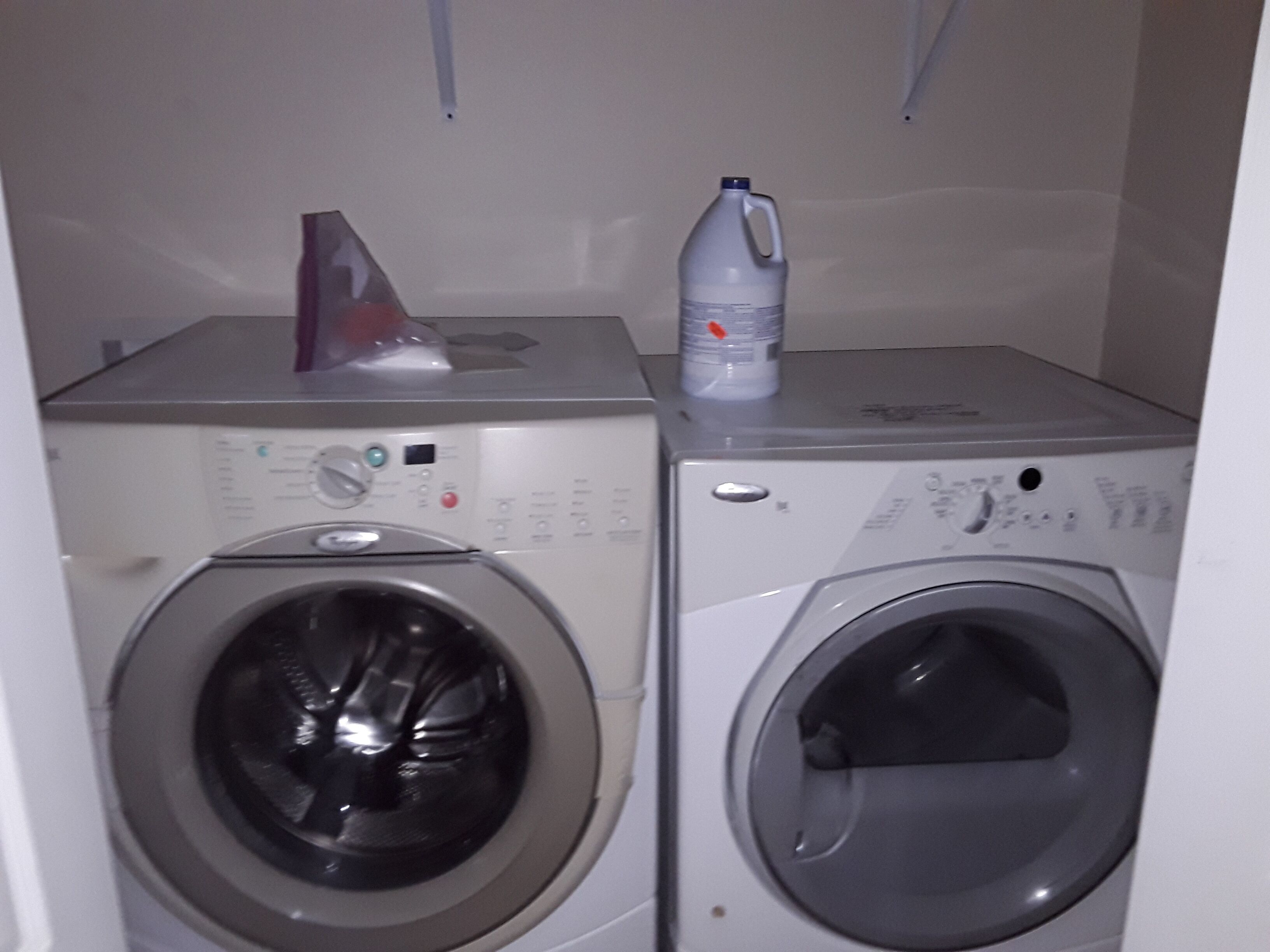 Two stacked washing machines with control panels, a red object on the top left, and a white bottle on the top right.