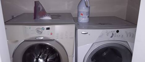Two stacked washing machines with control panels, a red object on the top left, and a white bottle on the top right.
