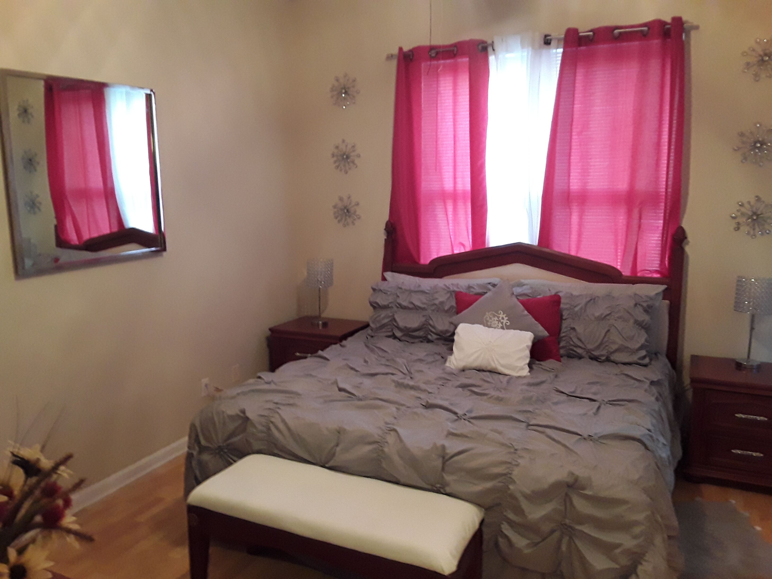 Une chambre à coucher avec un lit, une table de chevet, un miroir et une fenêtre avec des rideaux.