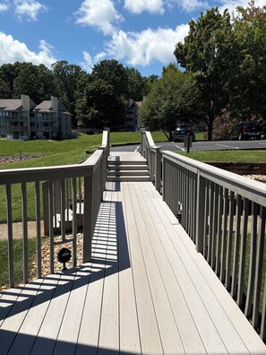 A wooden deck with railings, leading to a building with multiple balconies.