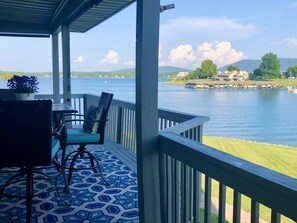 A covered outdoor area with a table and chairs, overlooking a body of water with boats and houses in the background. - Bernard's Landing, closest to lake, two comfortable king-size beds! (Moneta)