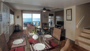 Een eetgedeelte met een glazen tafel, rieten stoelen en uitzicht op de oceaan.