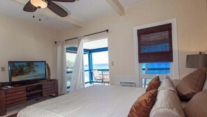 Een slaapkamer met een groot bed, een televisie, een plafondventilator en uitzicht op de oceaan.