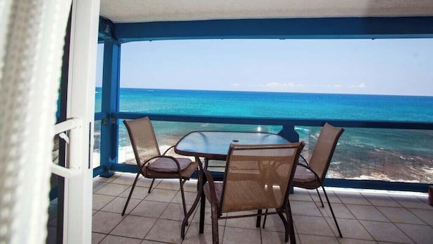Een balkon met een tafel en stoelen, uitkijkend op de oceaan.