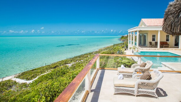 A beachfront property with a pool, outdoor seating, and a view of the ocean.