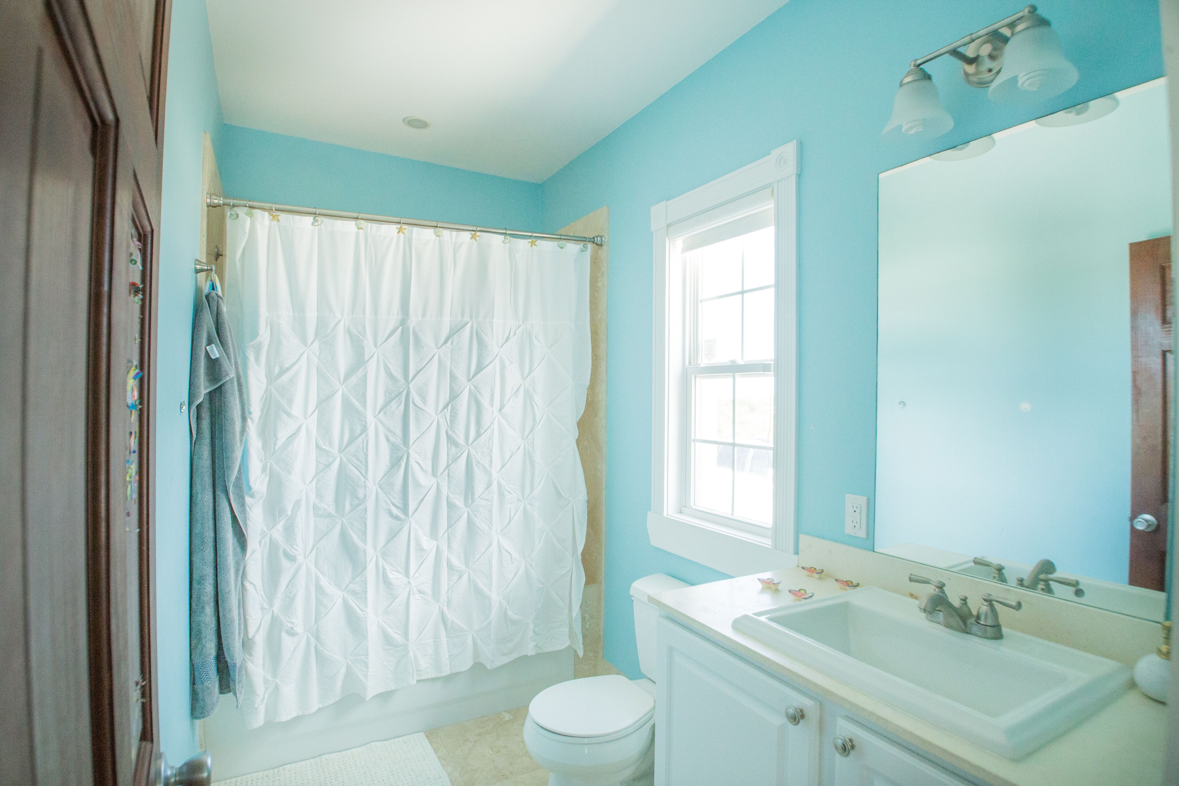 Une salle de bain avec des toilettes blanches, un lavabo blanc, un grand miroir et un rideau de douche.
