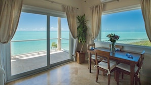 A room with a view of the ocean, a ceiling fan, a table with chairs, and a potted plant.