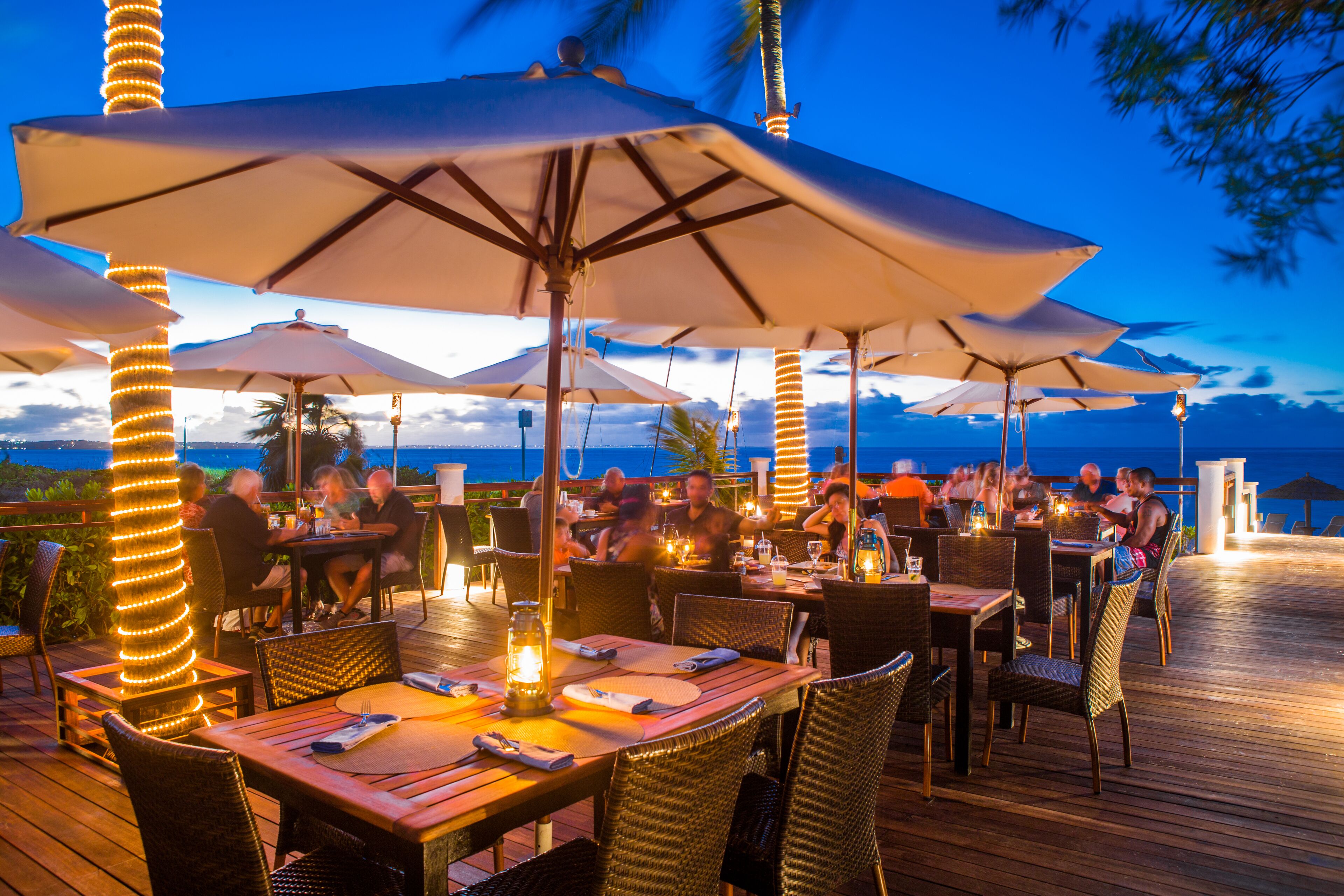 An outdoor dining area with tables and chairs, umbrellas, and string lights.