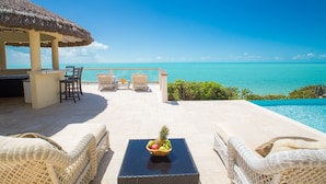 A beachside lounge with wicker furniture, a thatched-roof structure, and a view of the ocean.