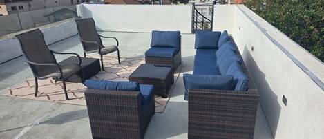 A rooftop terrace with wicker furniture and blue cushions.