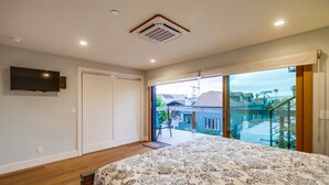Een slaapkamer met een groot bed, een aan de muur bevestigde televisie en een schuifdeur naar een balkon met uitzicht op de omgeving.