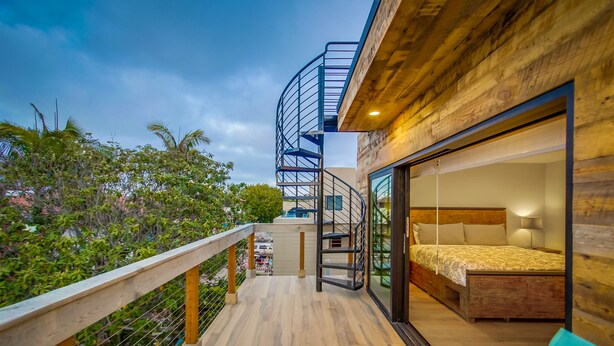 Een moderne slaapkamer met een houten hoofdbord, een bed met een beddengoed met een patroon, en een balkon met een houten vloer en hekwerk.