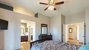 A bedroom with a bed, a ceiling fan, a dresser, a mirror, and a TV mounted on the wall.