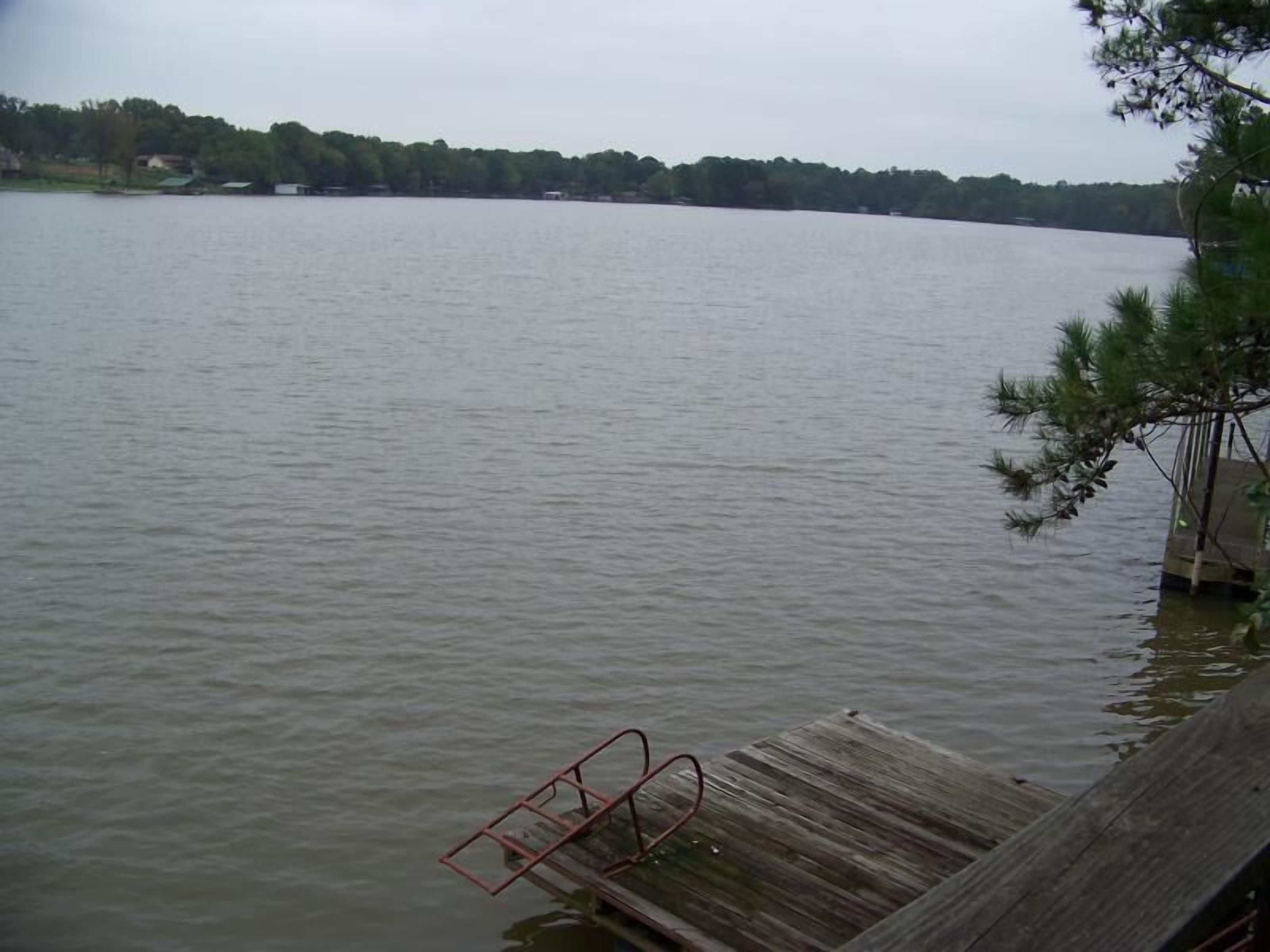 Une jetée en bois s’avançant dans un lac paisible, avec une rambarde en métal.