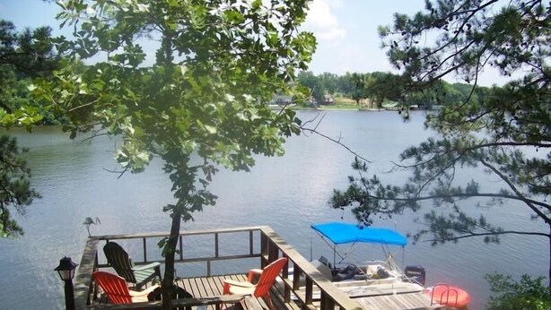 Una terraza de madera con sillas y un paraguas azul, con vistas a un lago tranquilo.
