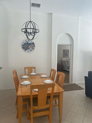A dining area with a wooden table and chairs, a decorative wall clock, and a doorway leading to another room. - OAK ISLAND COVE!   BEAUTIFUL POOL HOME with free Pool heat and Wifi (Kissimmee)