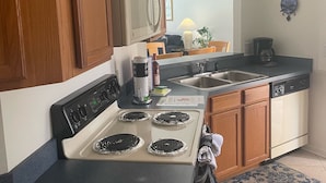 Una cocina con armarios de madera, microondas, estufa de cuatro quemadores, pileta y cafetera.