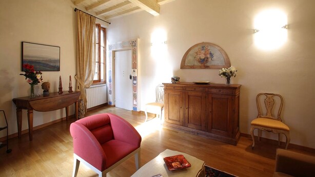 A spacious living room with wooden flooring, a red armchair, a wooden cabinet, and a painting on the wall. - CasaCaterina, in the Heart of the Old Center of Florence (Firenze)