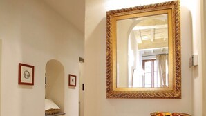 A hallway with wooden flooring, a white wall, and a large mirror with a decorative frame. - CasaCaterina, in the Heart of the Old Center of Florence (Firenze)