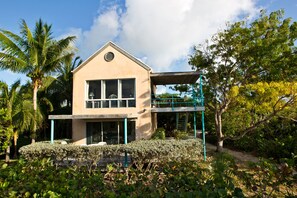 Ein zweistöckiges Haus mit Balkon, umgeben von üppiger Vegetation und Palmen.