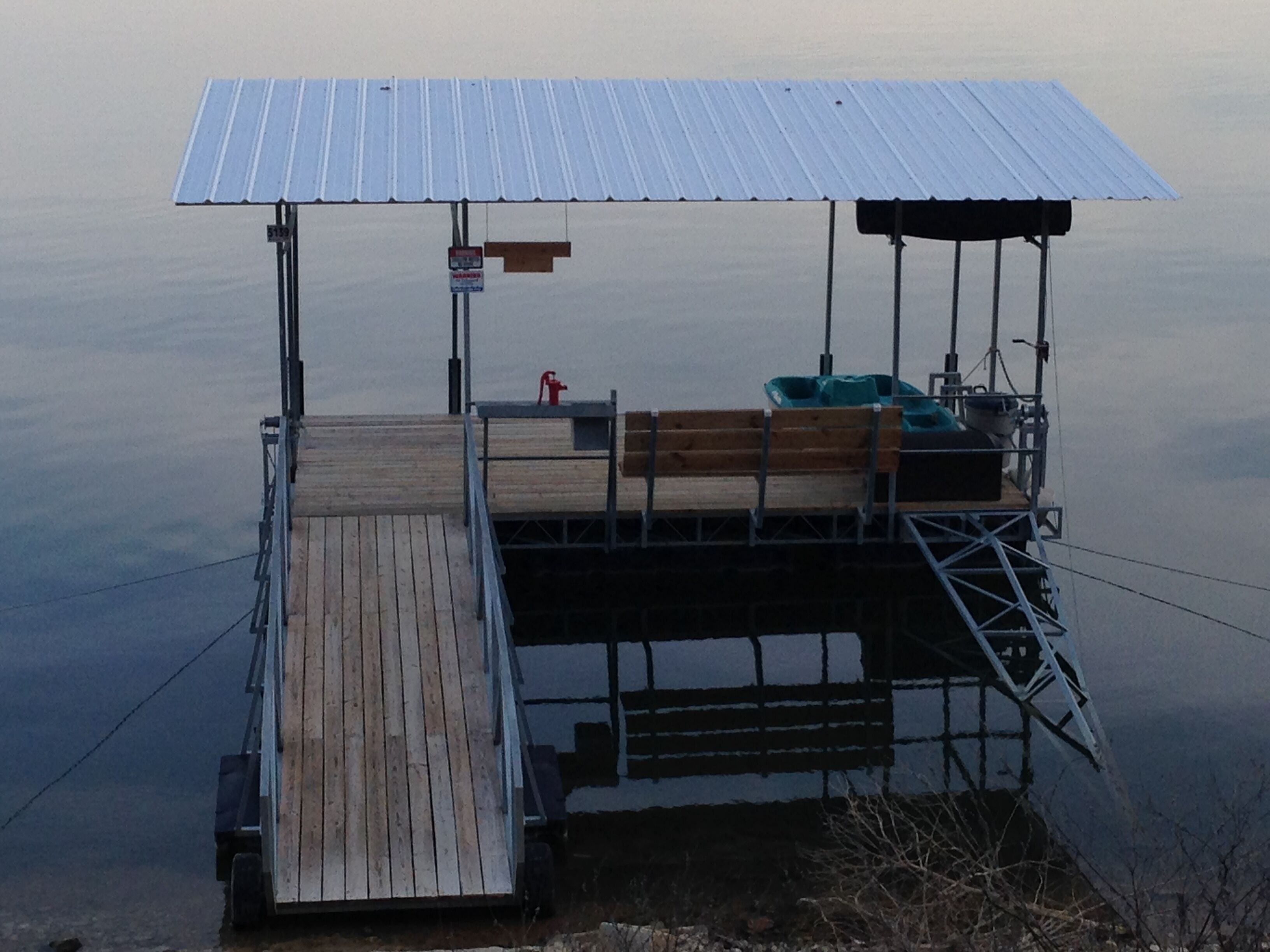 A dock with a metal roof, wooden benches, and a small boat.