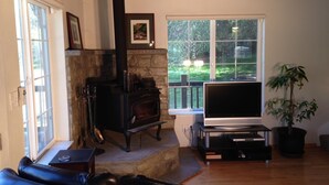 A living room with a stone fireplace, a television, a sofa, and a large window with a view of greenery.