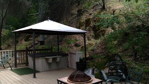 A wooden deck with a covered seating area, a hot tub, and a fire pit.