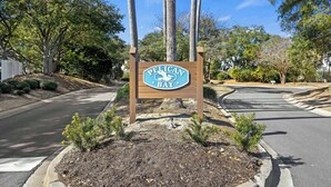A sign for Pelican Bay with a clear road and trees in the background. - The FAMILY Spot in Wild Dunes - Walking Distance to Beach - Pool Access (Isle Of Palms)