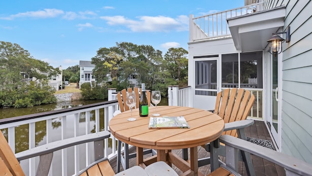 A wooden deck with a round table and chairs, a bottle of wine, and a magazine. - The FAMILY Spot in Wild Dunes - Walking Distance to Beach - Pool Access (Isle Of Palms)