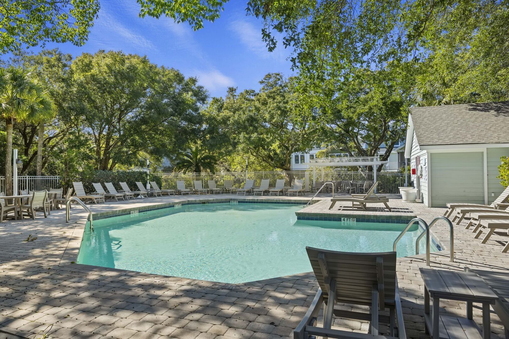 A rectangular pool with a tiled edge, surrounded by lounge chairs and a covered seating area.