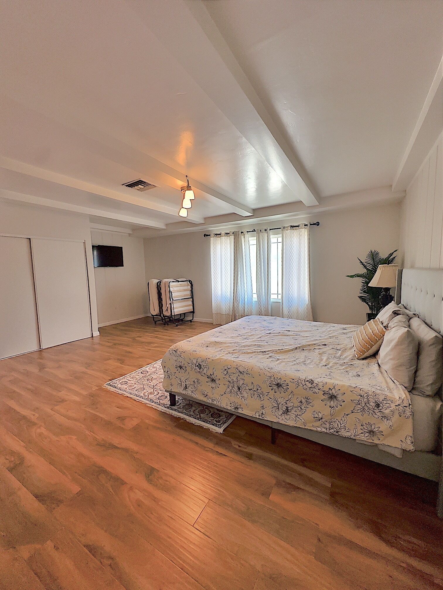Ein geräumiges Schlafzimmer mit einem großen Bett, Holzboden, Deckenventilator und einem an der Wand befestigten Fernseher.