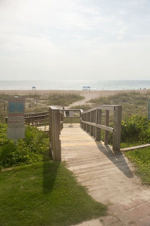 Une promenade en bois mène à une plage où un panneau avertit de la présence de courants de contre-rivage.