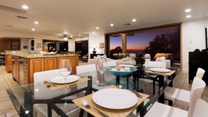 A modern dining area with a glass table, white chairs, and a view of the sunset.
