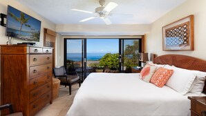 A bedroom with a bed, a dresser, a chair, a ceiling fan, and a view of the ocean.